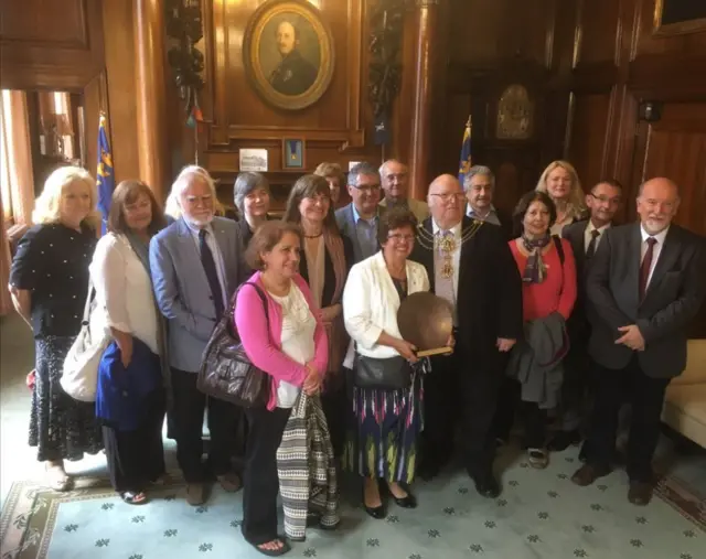 The group of people with a circular plate shaped plaque on a stand.