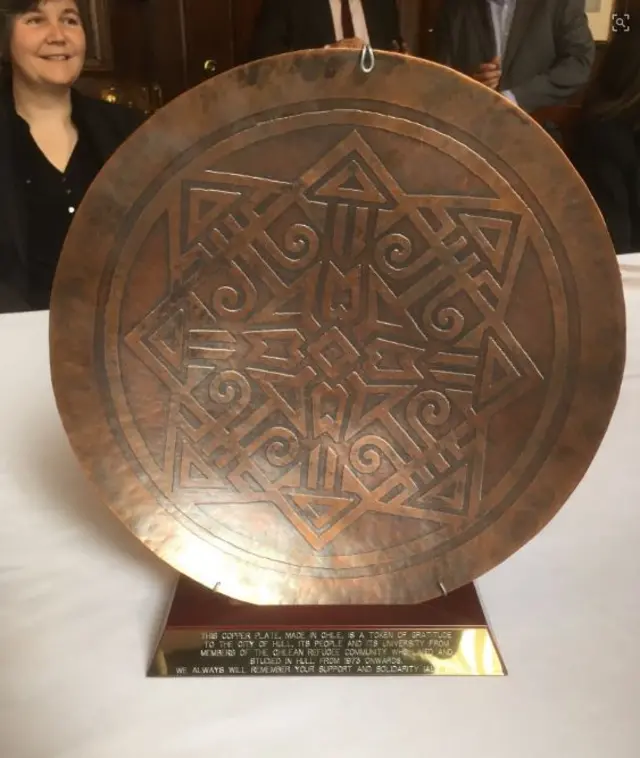 The bronze coloured plaque with an Aztec design on it.