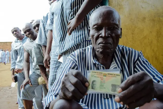A Kenyan inmate shows his ID as he waits in line to cast his vote in Kisumu, on Lake Victoria