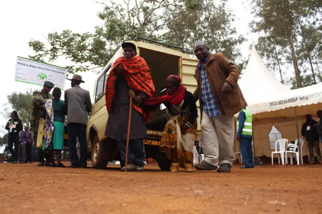 Elderly people are aided out of a vehicle near a voting station