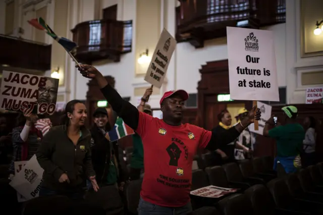 Protesters hold signs calling for President Zuma to go