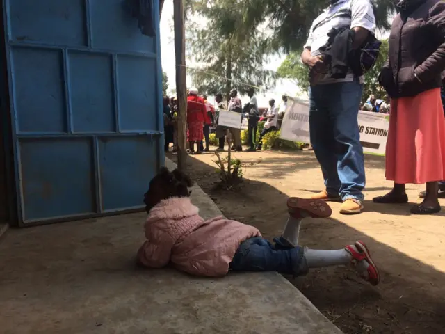 A child lies on her stomach outside the voting station where delays have been caused by incorrect ballot papers.