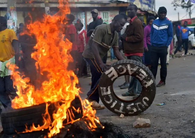 A protesting resident of Kibera slum pushes a tire sketched with the message "Justice Peace" on a road in Nairobi on August 9, 2017, during protests against Kenya"s national election results.