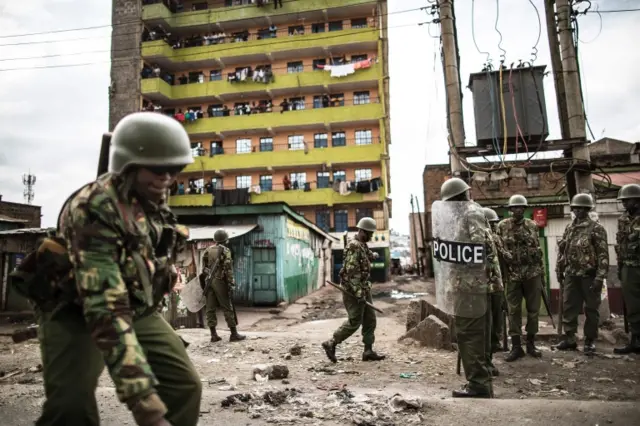 Kenyan Administration Police officers are watched by residents as they patrol in the Mathare Slum of Nairobi on August 9, 2017