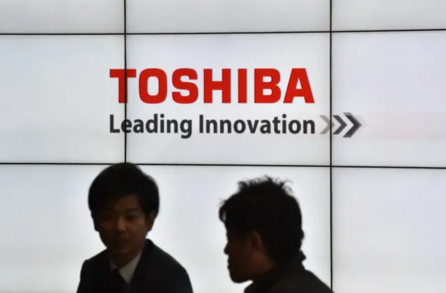 Men stand in front of a Toshiba logo