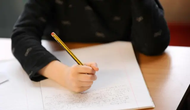 Generic shot of pupil, seated at desk, writing in exercise book