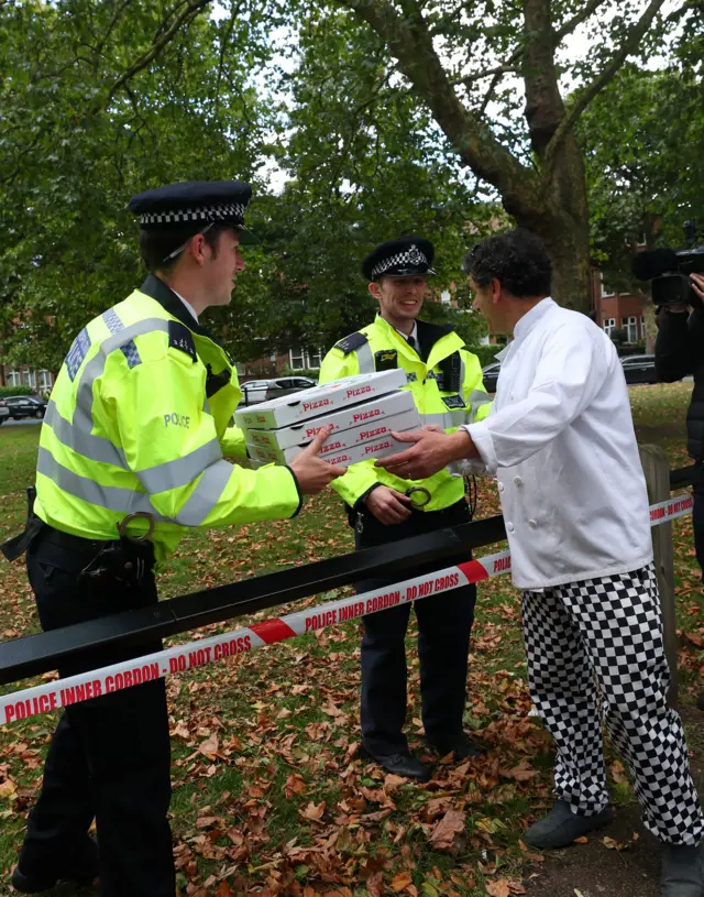 chef hands pizza to police officers behind corden