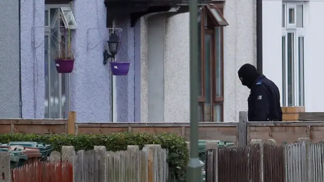 A masked police officer enters a property in Sunbury-on-Thames