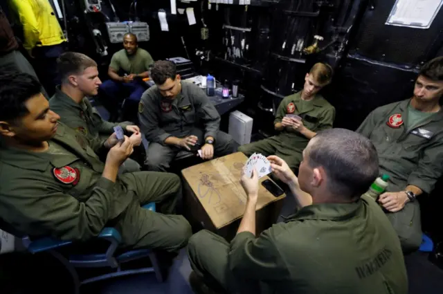 Marine Corps crew chiefs and maintenance personnel play cards in a room near the flight deck of the USS Kearsarge as the vessel handles some of the evacuation of U.S. military personnel