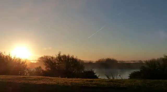 The sun coming up over s field with mist on a lake.