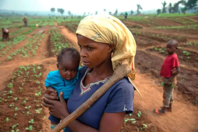 A mother holds her baby in the field where she is working