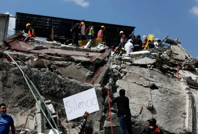 A man holds up a sign that reads "silence" as rescue personnel look for people underneath the rubble of a collapsed building after an earthquake hit Mexico City, Mexico 19 September 2017.