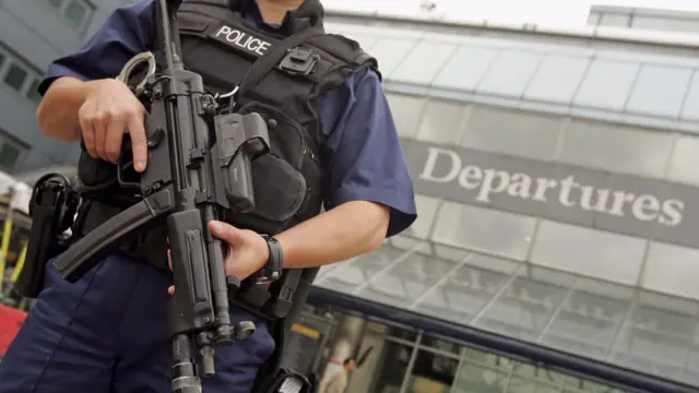 An armed British police officer patrols outside of Heathrow Airport