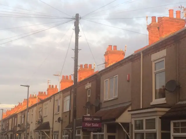 The sun coming up over the roof tops of a row of terraced houses.