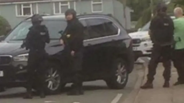 Armed police by a black BMW car.