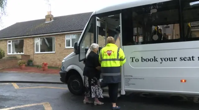 Woman being helped onto minibus.