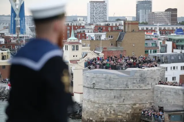 A sailor looks out at spectators on the Round Tower as HMS Queen Elizabeth, the UK"s newest aircraft carrier, arrives in Portsmouth for the first time