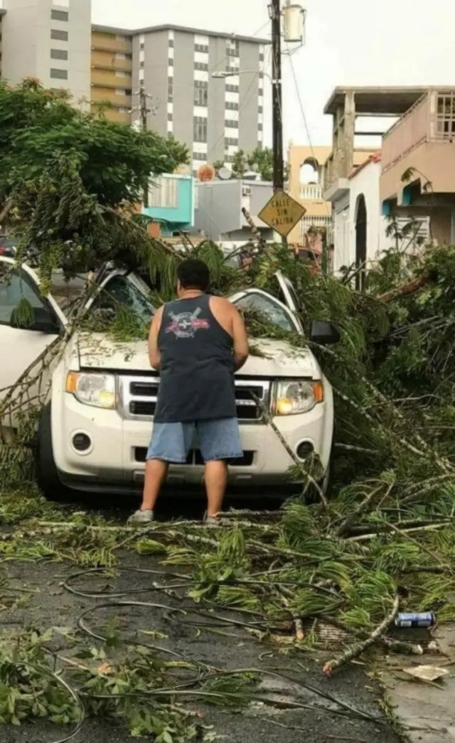 A man removes debris that damaged a car in San Juan, Puerto Rico