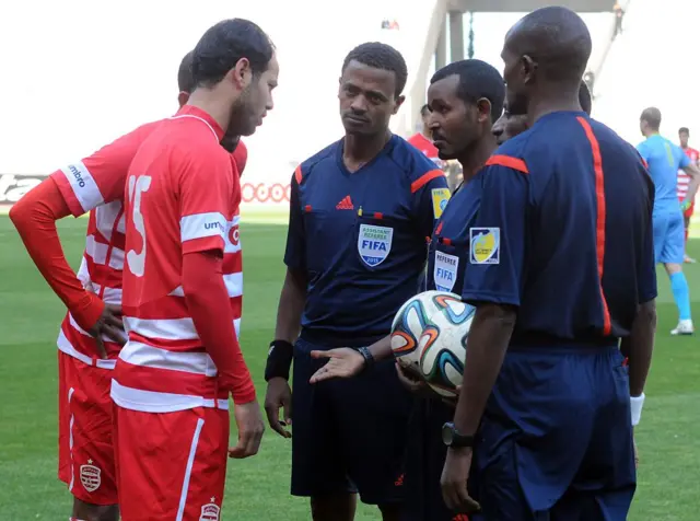 Tunisian Club African football team captain Zouheir Dhaoudi (L) speaks with Ethiopian referee Bazezew Belete (C-R) who declared Club African the winners of their CAF confederation cup football match against Nigerian team Dolphin Port Harcourt at the Rades Stadium, on the outskirts of Tunis, after the Nigerian team were force to forfeit after arriving one hour late for kick-off due to visa-related issues at the airport on March 14, 2015