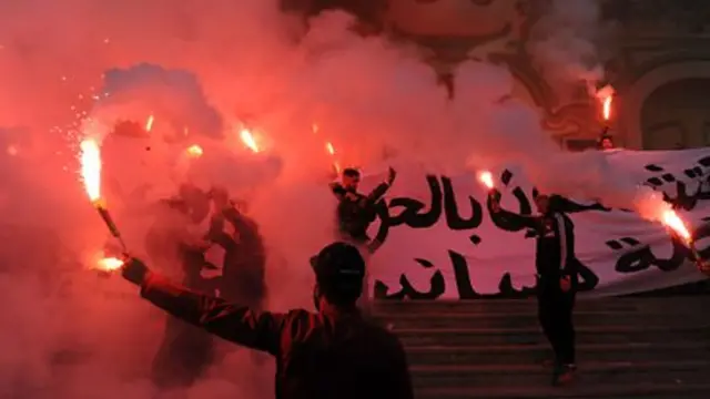 Tunisians carry flares and shout slogans against the government in Tunis on 14 January