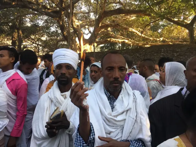 Timkat festival - two men stand together in the crowd, one holds  a candle