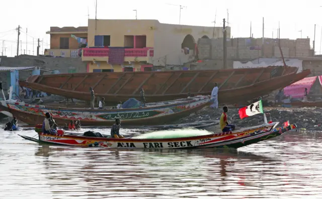 Fishermen sail by a pirogue (back) at the port of Saint-Louis 14 September 2006