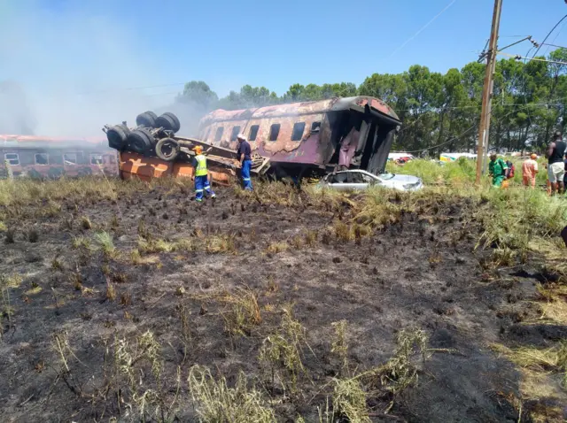 Two rescue workers stand by an overturned truck and burnt-out train