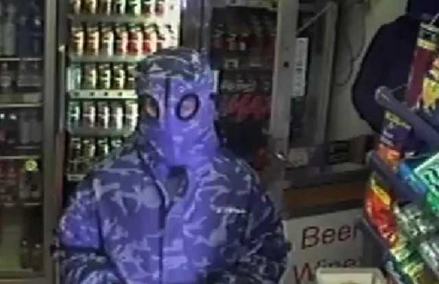 A man wearing a purple camouflage coat with goggles in the hood.