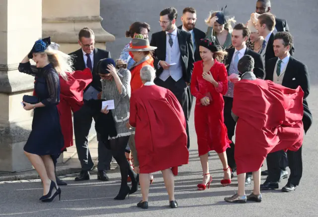 Wedding guests hold onto their head wear in the windy conditions as they arrive for the wedding