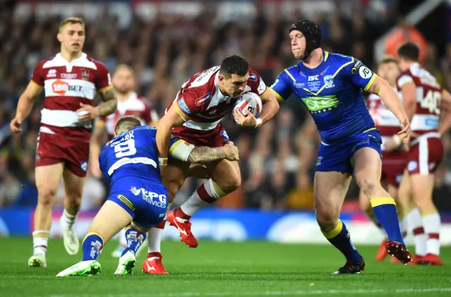 Ben Flower of Wigan Warriors is tackled by Daryl Clark of Warrington