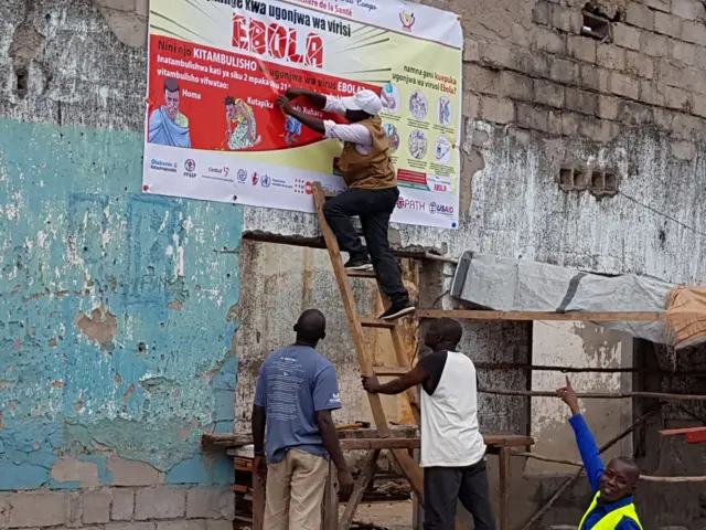 Workers fix an Ebola awareness poster in Tchomia, Democratic Republic of Congo, to raise awareness about Ebola in the local community - 9 October 2018