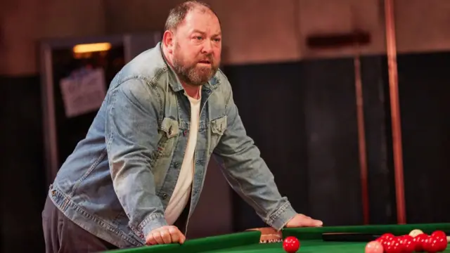 Mark Addy as Bobby Spokes leaning on a snooker table