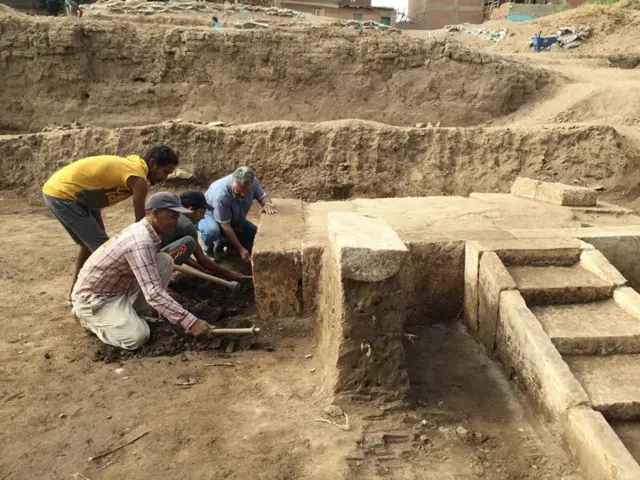 Archaeologists crouch down next to their discover