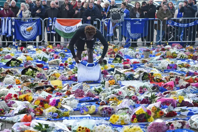 A Leicester City youth player places a shirt among the sea of tributes