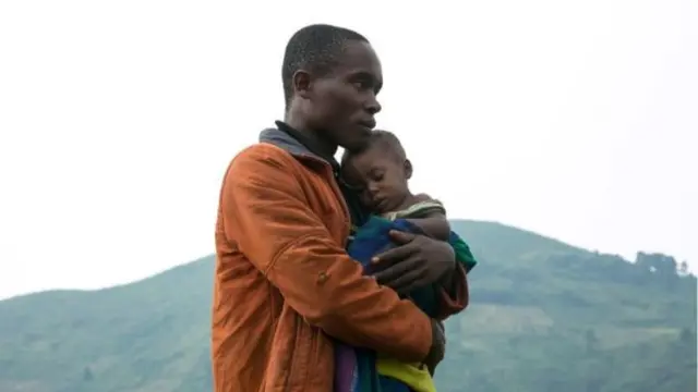 A man holds his child having crossed the border into Uganda as refugees