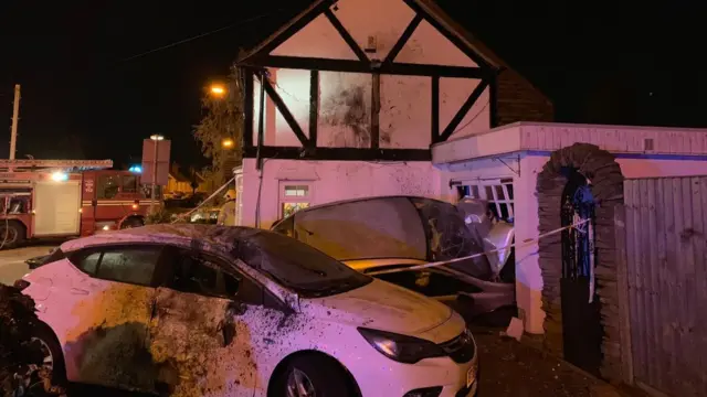 The two cars and side of house after being hit by the third car