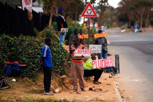 Job seekers wait on the side of a road holding placards reading their specialisation, on August 4, 2017 in Johannesburg, South Africa. Africa's most advanced economy unexpectedly contracted in the first quarter of this year, slipping into its first recession since 2009.