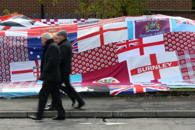 Football supporters walk past flags outside Burnley's Turf Moor stadium