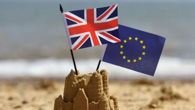 A sand-castle, with the Union and European Union flags flying from its top,