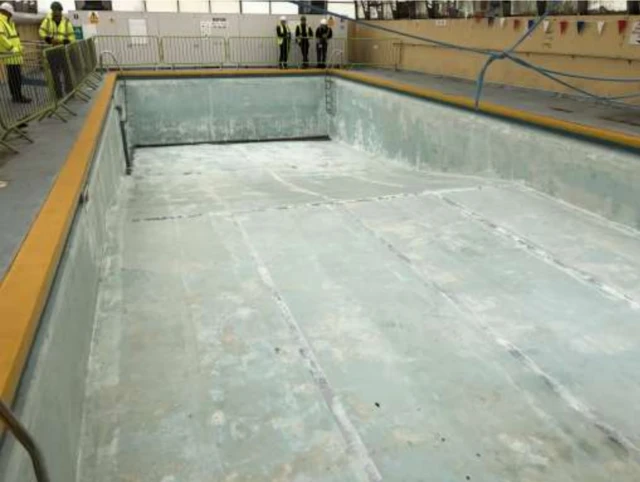 Interior view of Millom Pool with water drained out and inspectors looking at it