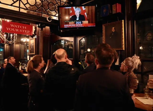 Members of the public watch a live broadcast of British Prime Minister Theresa May"s speech diplayed on a television next to a picture of former British Former Minister Benjamin Disraeli at the Red Lion Pub on November 15, 2018 in London