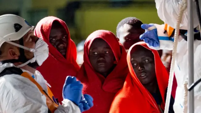 Migrants wrap themselves in orange blankets after being rescue from the sea