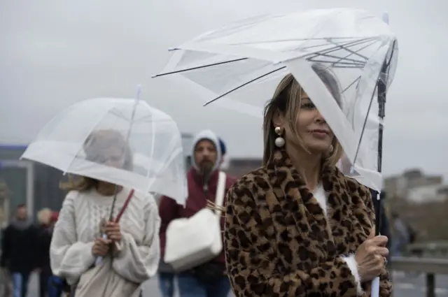 People with umbrellas in the wind on Westminster Bridge in London