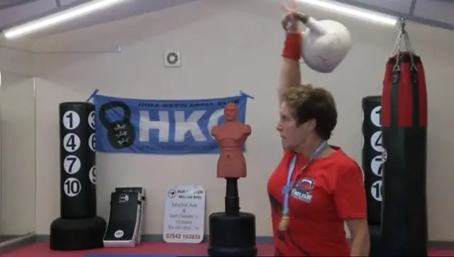 June Sawdon lifting a kettlebell while wearing her medal