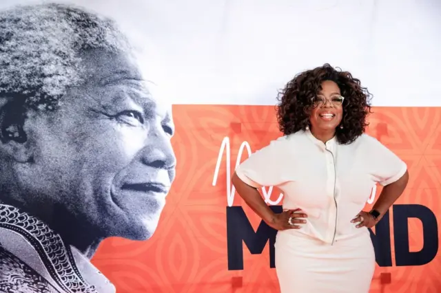 Oprah Winfrey poses on the red carpet next to a banner depecting late former South African president Nelson Mandela, as she arrives to attend an event to mark 100 years since the birth of Nelson Mandela, at the University of Johannesburg, Soweto Campus, in Johannesburg on November 29, 2018.