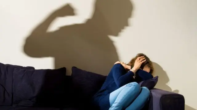 Woman cowering with shadow of man raising fist on the wall behind her