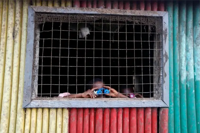 Two curious children peep through a window with toy binoculars in Ghana.