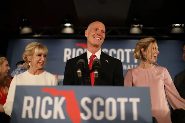 Florida Governor Rick Scott takes to the stage as he stands with his wife, Ann Scott, (L) and daughter Alison Guimard (R) during his election night party