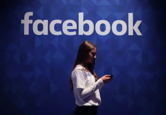 woman using her phone under a Facebook logo