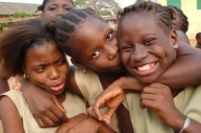 Three triends in Porto Novo, Benin, hug each other while one kisses another.